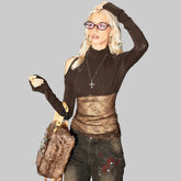 Person wearing a brown top and black pants with a fur bag, standing in front of a wall with graffiti.
